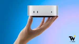 A person holding a compact silver Apple Mac Mini desktop computer in the palm of one hand against a blue gradient background.